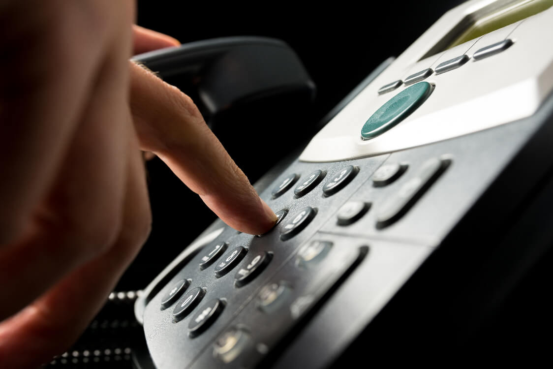 A hand dialing a desk telephone.